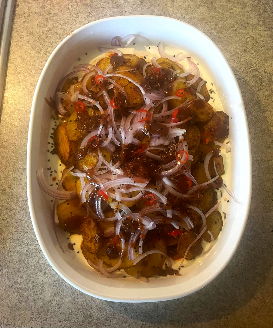 A large dish of cooked potatoes with various spices and slices of onion and chilli on