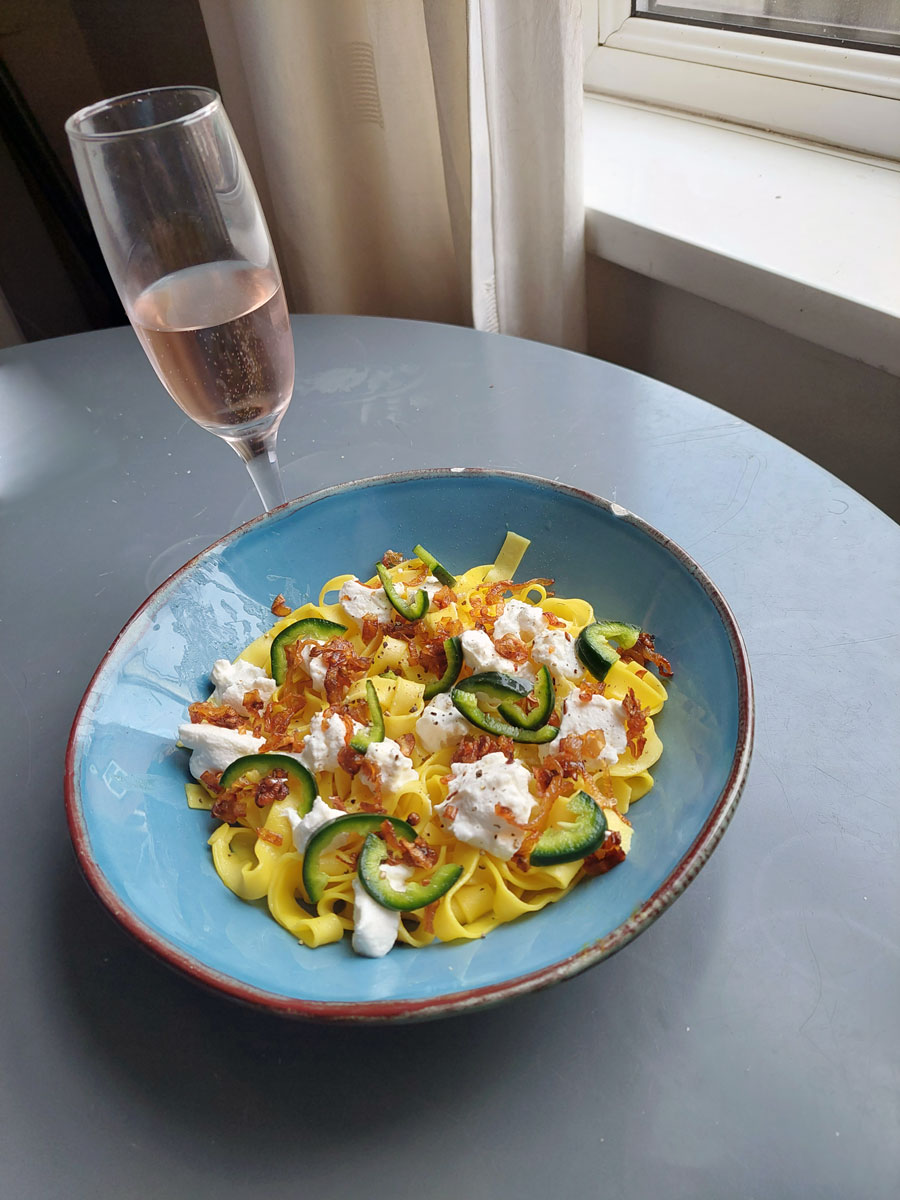 A serving of saffron tagliatelle in a blue dish in front of a flute of sparkling wine
