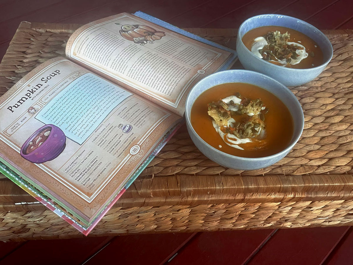 Two bowls of pumpkin soup beside a cookbook which is open at the recipe for "Pumpkin Soup"