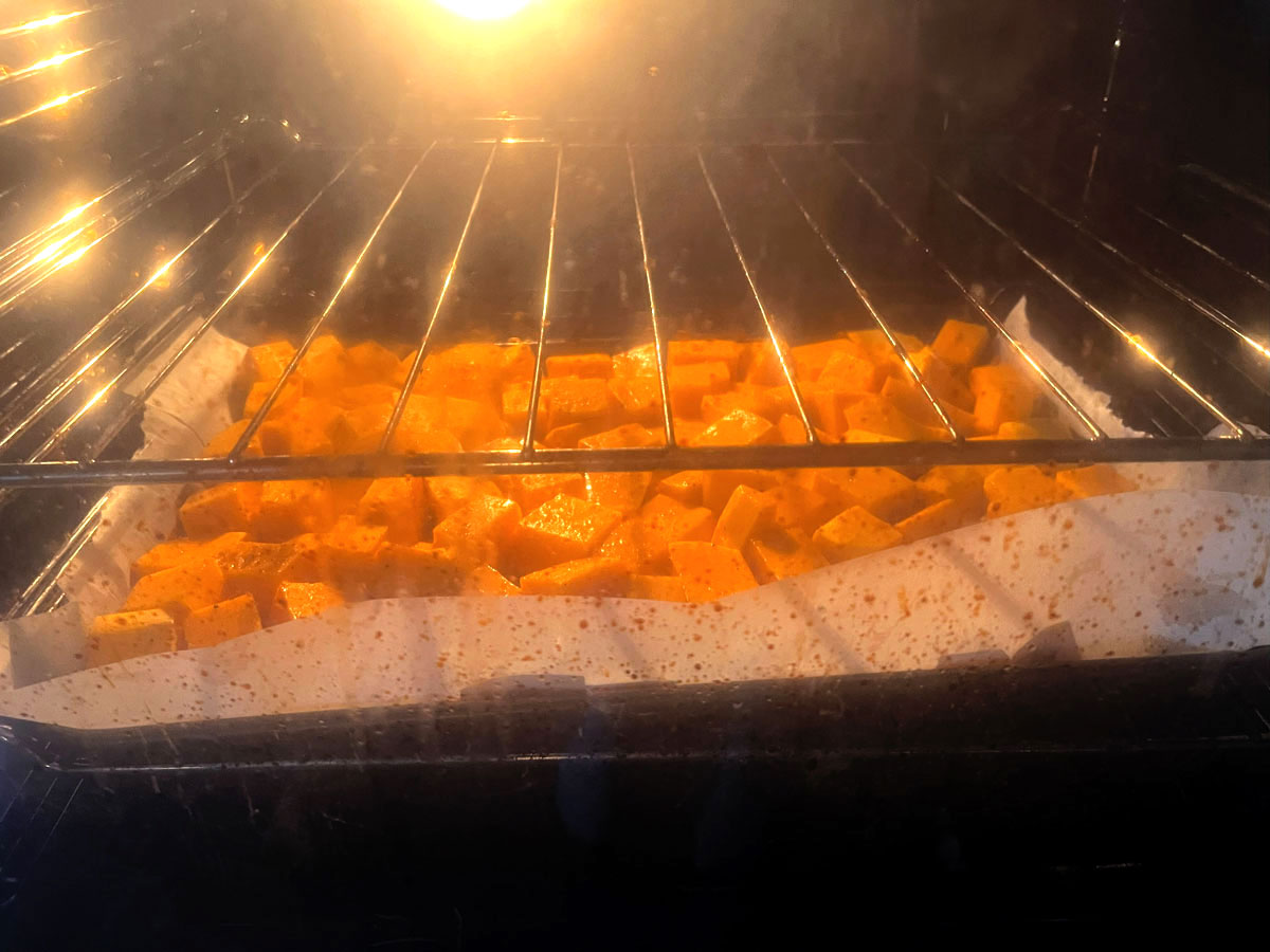 A baking tray in an oven, lined with baking paper, with diced pieces of pumpkin on it