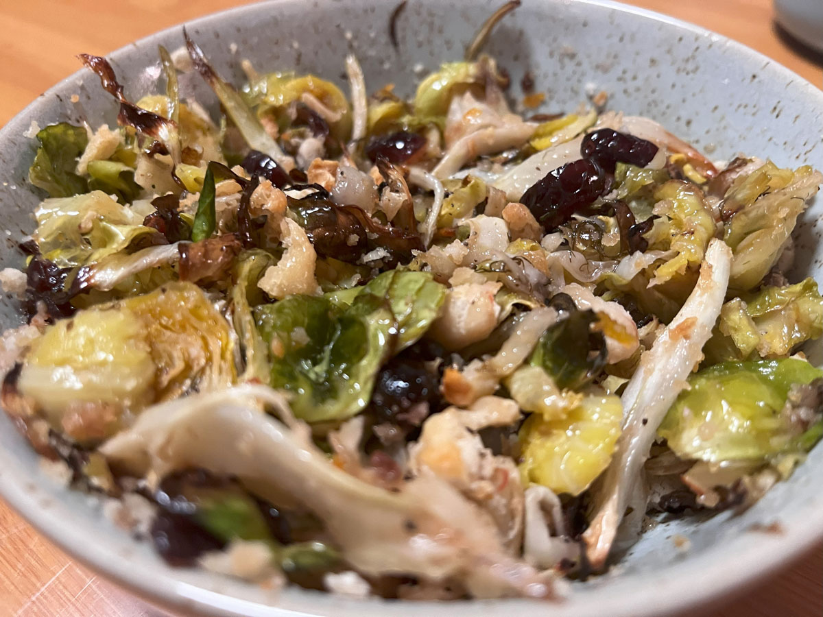 semi-focused shot of baked salad with bean crumble mixed through shredded vegetables and cranberry dressing in blue speckled bowl