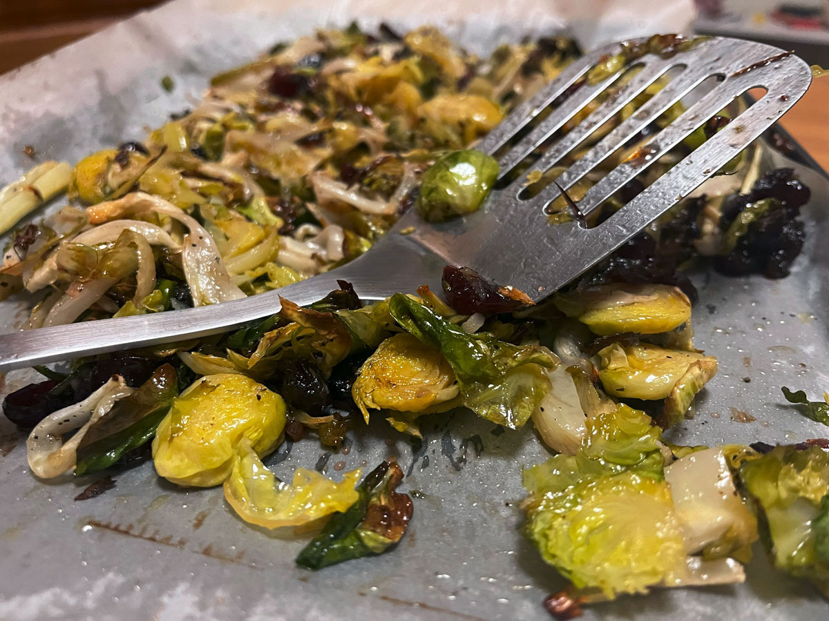 stylistic shot of cooked vegetables with cranberry dressing mixed through, being held up by spatula
